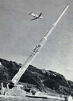 A photo of a large artillery-style gun aimed upwards, with a plane flying overhead.