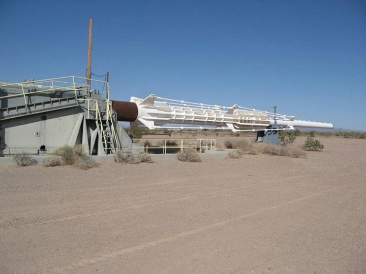 A white artillery cannon lies horizontally on a flat desert landscape.