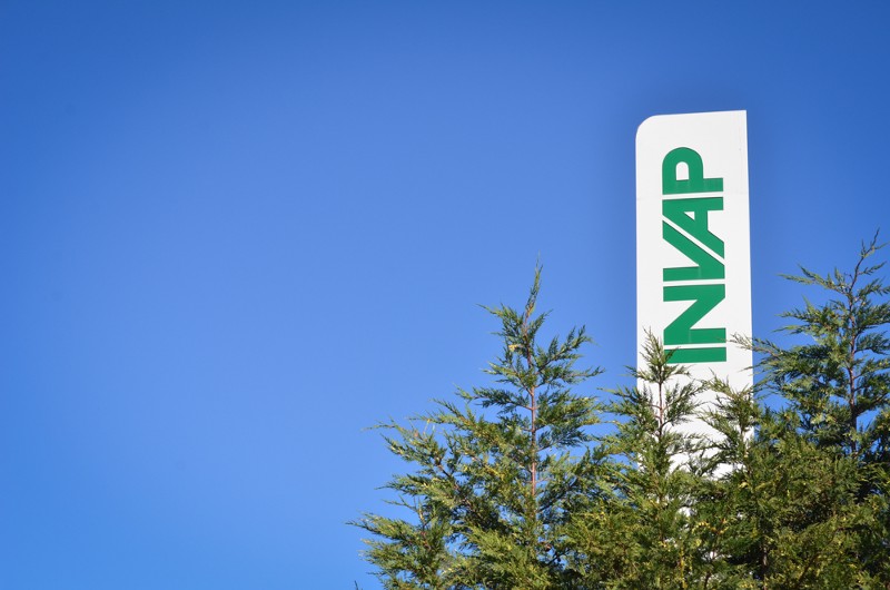 The INVAP logo emerges on a sign from a treeline.