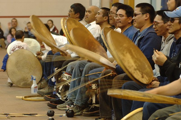A row of people drumming on large drumskins.