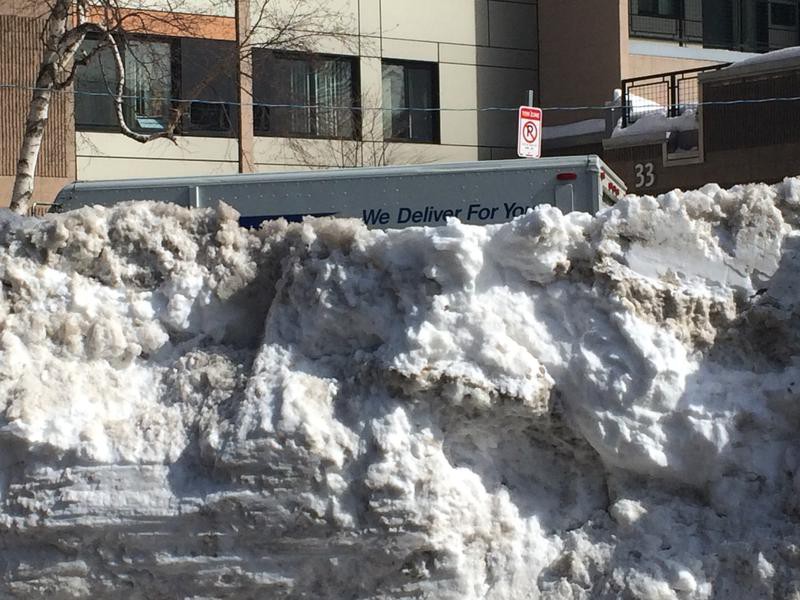 A Postal Service van buried beneath a high snow drift.