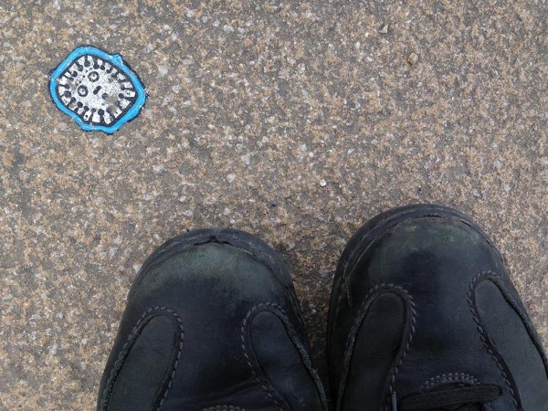 A piece of chewing gum on the sidewalk, colored in with marker pens to show a face surrounded by a blue outline.