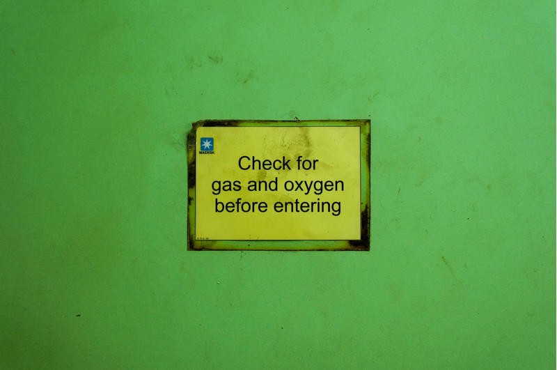 A warning sign on a wall. It reads: "Check for gas and oxygen before entering."