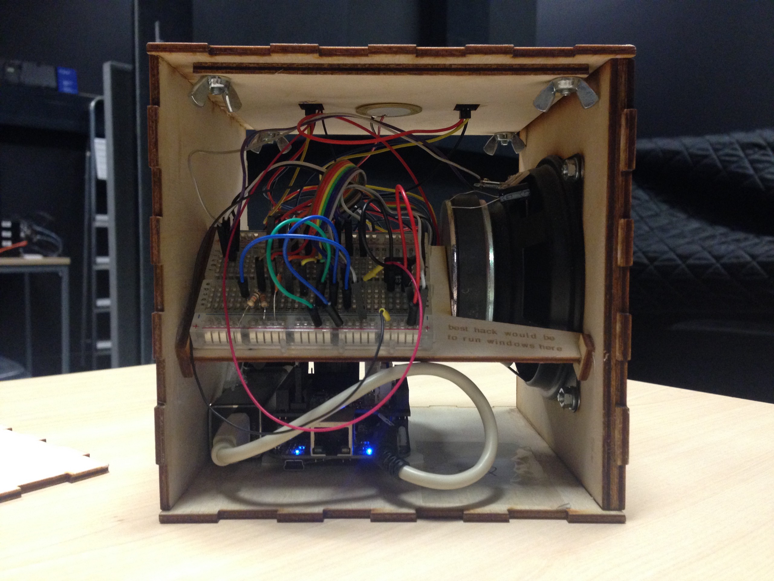 A wooden box speaker is open. Inside is a mess of wires and circuitry, connected to the speaker cone.
