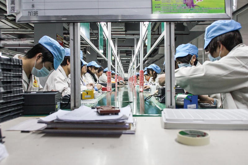 People in a factory work a manufacturing line for phones.