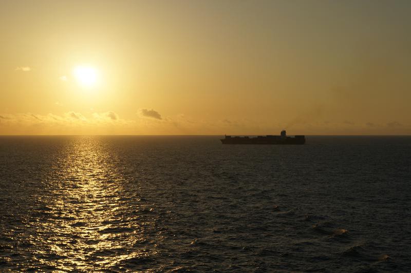 A container ship sails across the horizon of the sea.