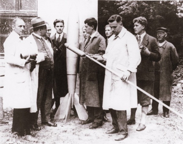 A group of people inspect small rockets.