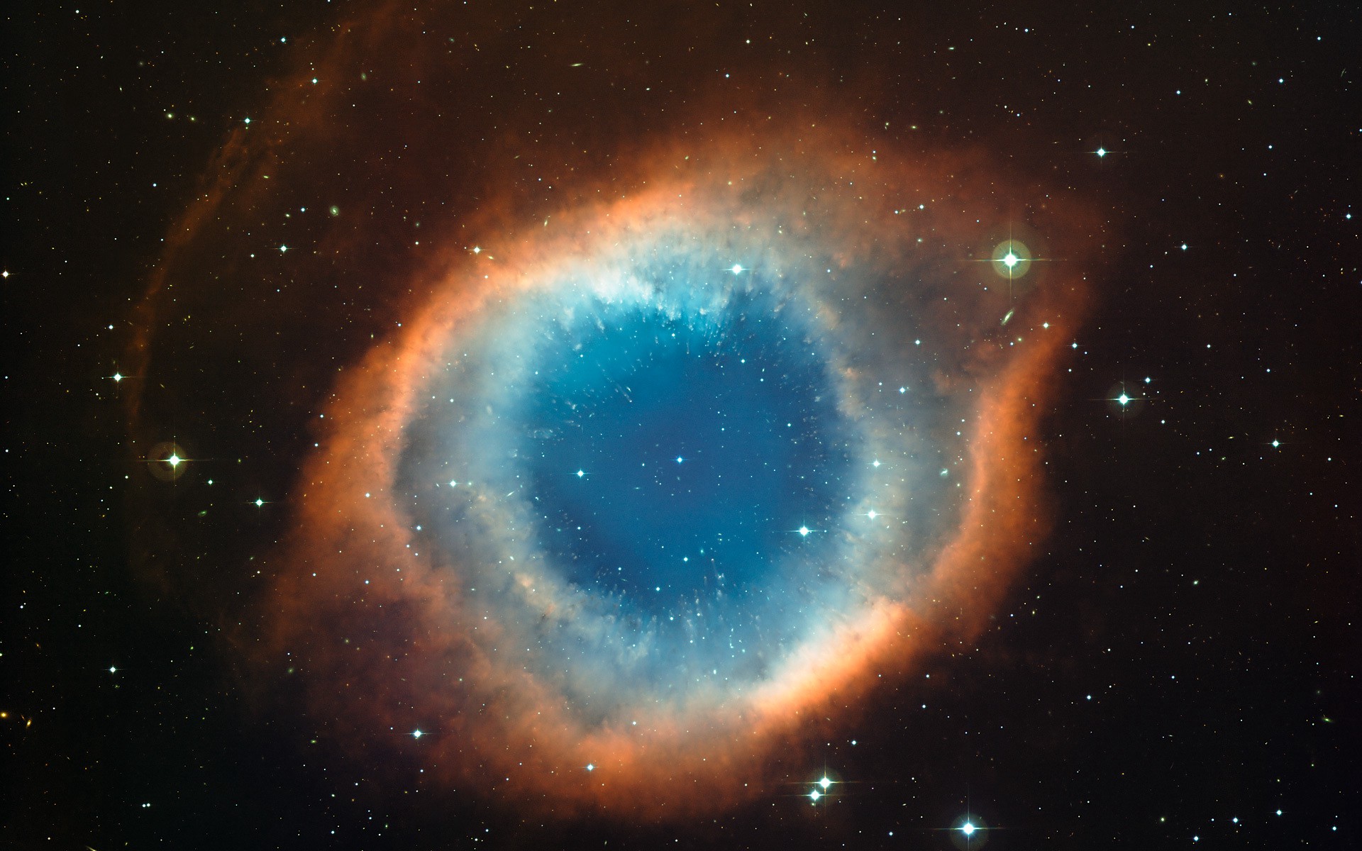 A circular nebula in space with a blue center surrounded by an orange rind, surrounded by stars.