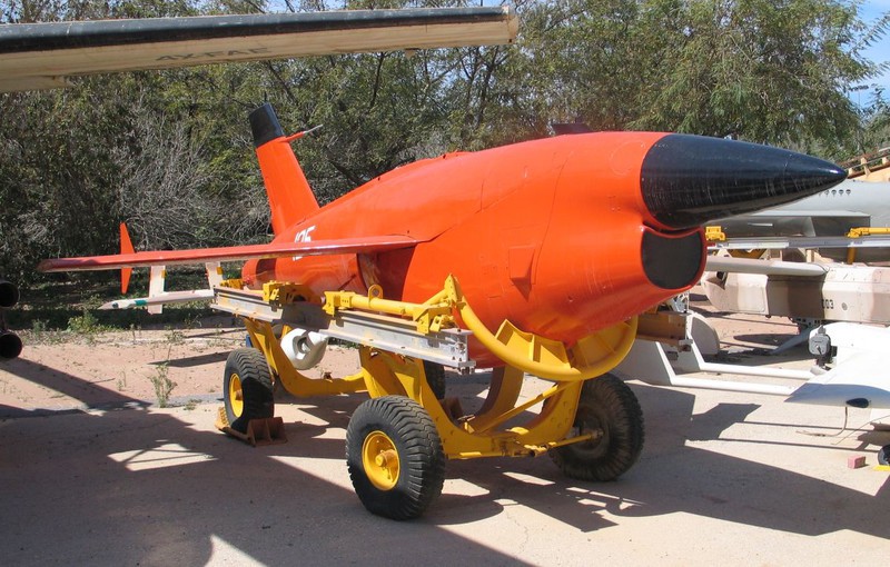 A bright red rocket drone resting on a wheeled dolly in a lot.