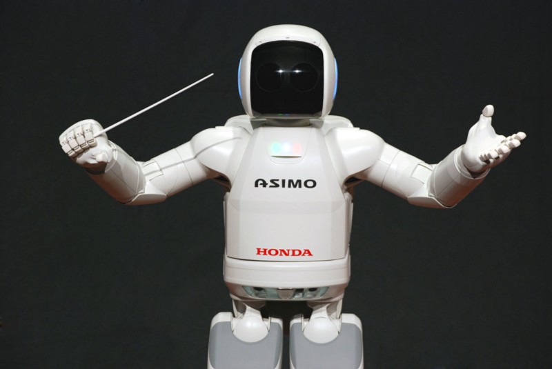 Honda's humanoid Asimo robot holding a conductor's baton, conducting an orchestra.