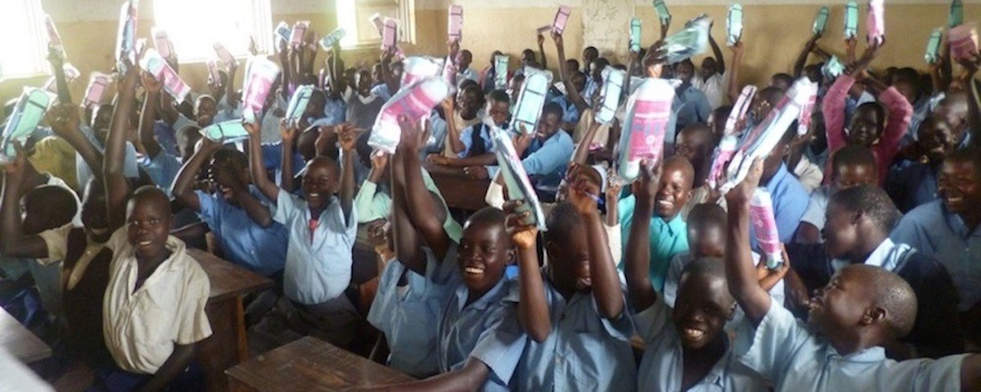 Children in a classroom holding aloft their menstrual kits.
