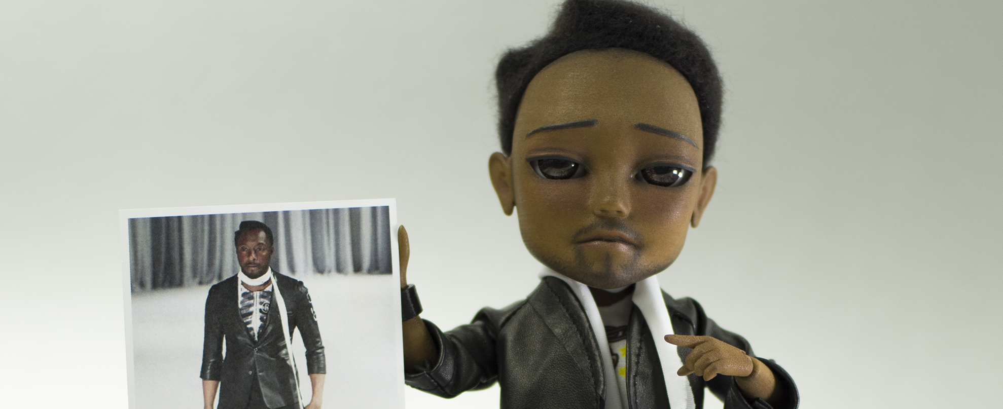 A doll that looks like The Black Eyed Peas Will.i.am holds up a photo of the real Will.i.am