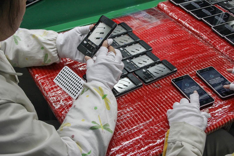 A person in a clean suit inspects phones on a manufacturing line.