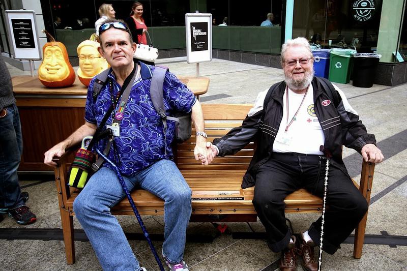 Two men holding hands, sitting on a bench.