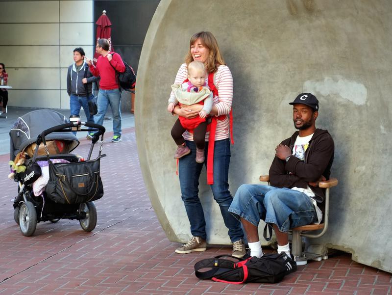 A man sits in a chair inside the reflective concrete dish, while a woman stands beside him holding a baby.
