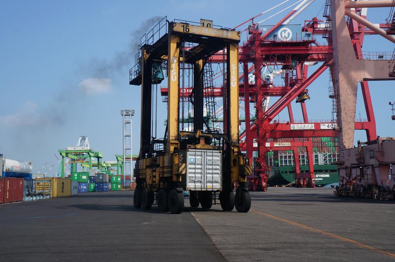 A large motorized crane on wheels moves around a container port.