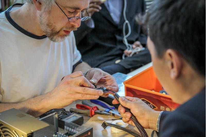 Two people help each other rewire an electronic device.