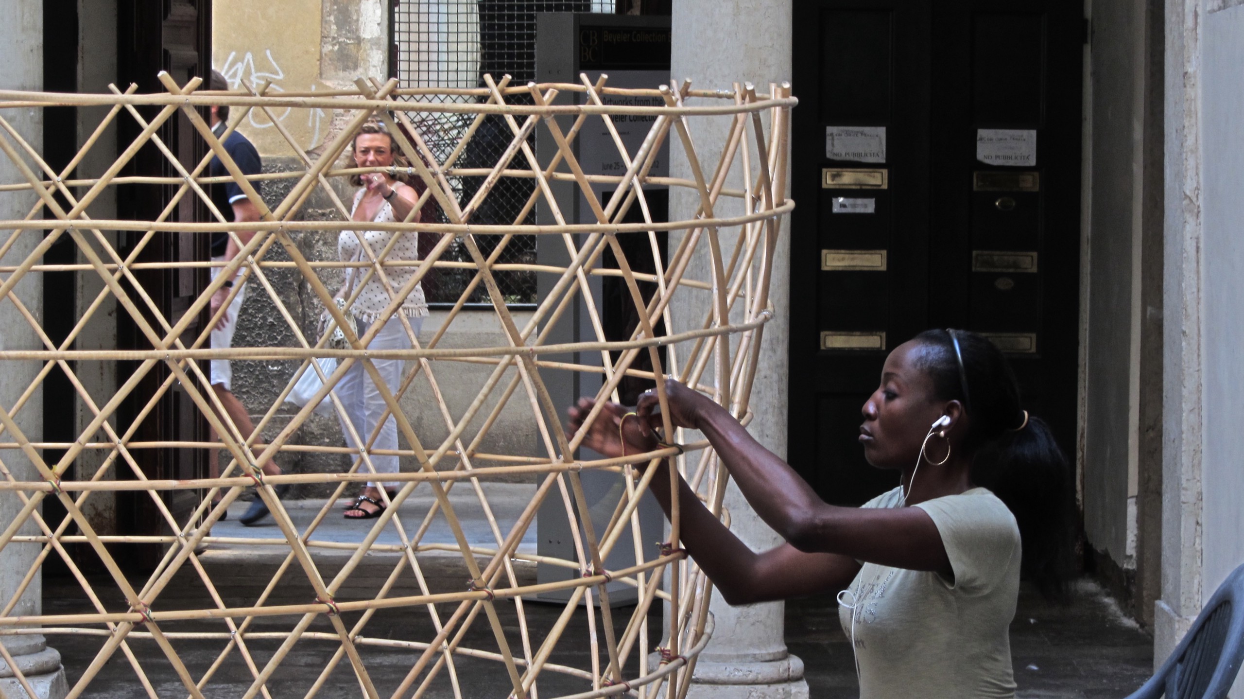 A woman interweaves bamboo canes to construct a large tower structure.