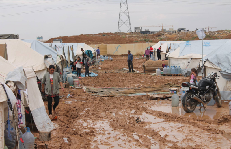 A refugee camp made up of tents along a mud and dirt avenue. It looks like a horrible place to be.