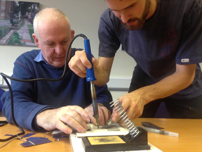 Two people fix a broken solar cell using a soldering iron.