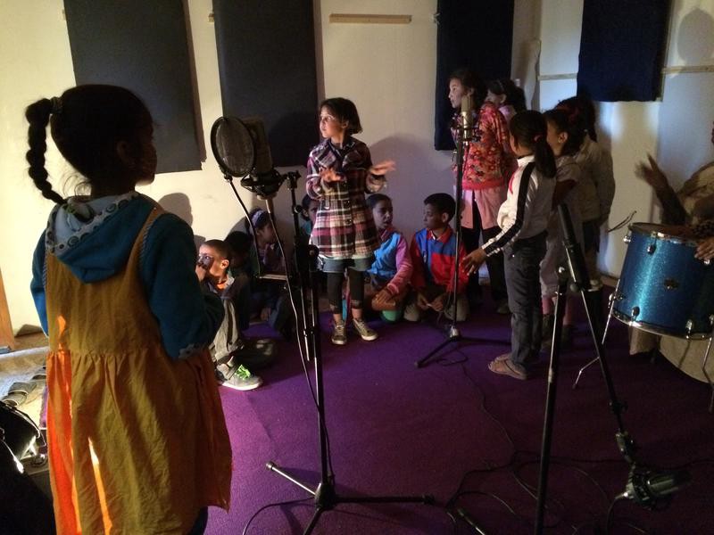 A group of children in a small recording studio, with instruments and microphones