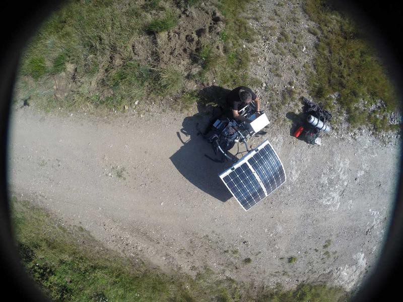 An aerial view of a man sitting on a chair, next to a big solar panel.