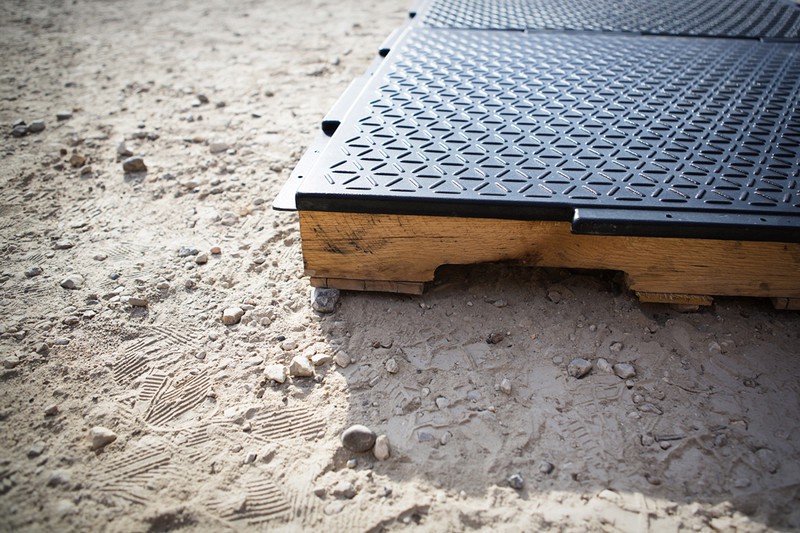 A rubber tread floor mounted on wooden runners lies on top of a dirt ground.
