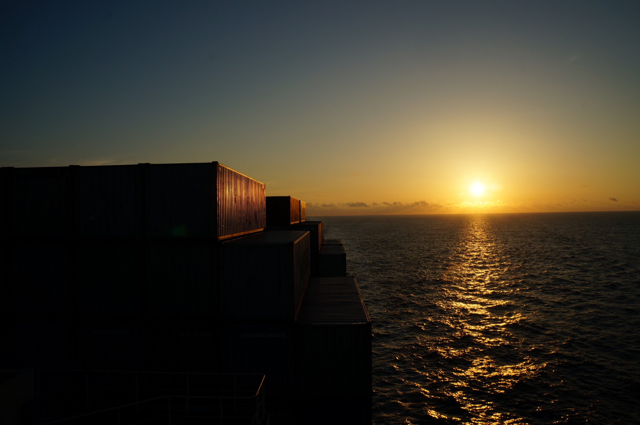 A container ship at sea, with the sunset in the distance.