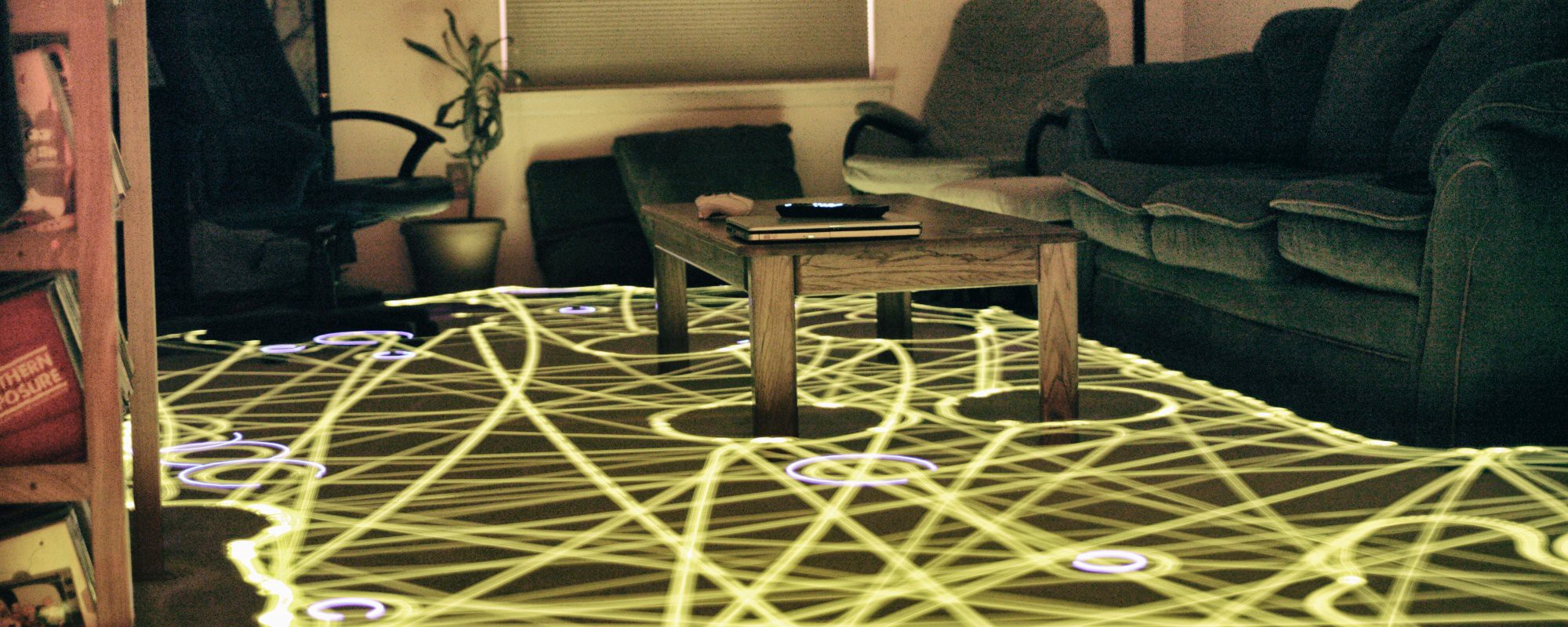 A timelapse photograph of a robot vacuum's trip around the lounge of a home, showing its path marked out as a trail of light.