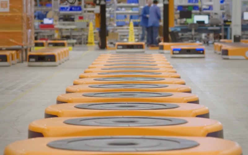 A line of huge circular floor robots, designed to ferry goods around a warehouse. The robots are emblazoned with Amazon branding.