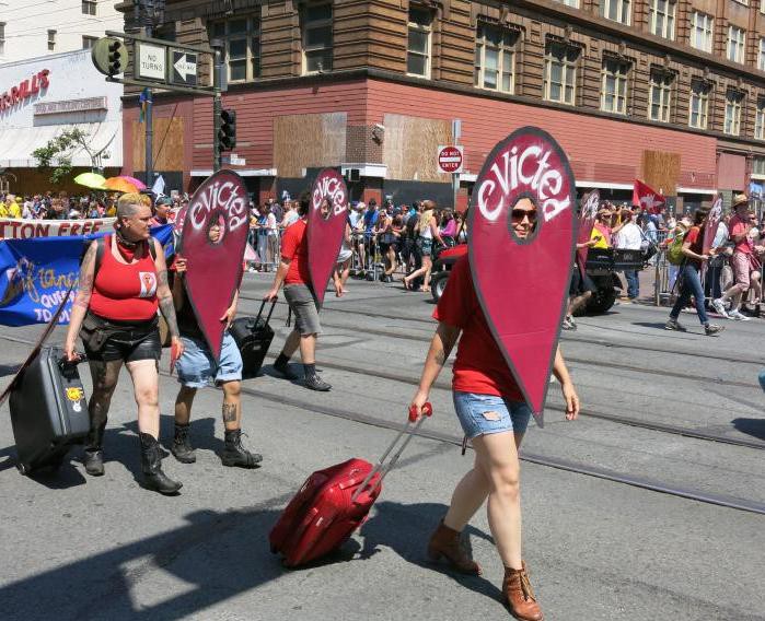 A group of protesters walk along a street while wearing costumes that say "evicted" on them.