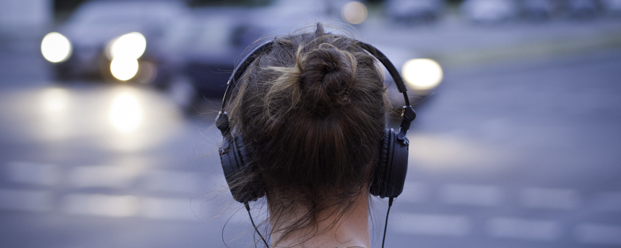 A woman wearing over-ear headphones walks down a street.