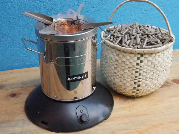 A cookstove on a table, next to a wicker basket containing fuel pellets.