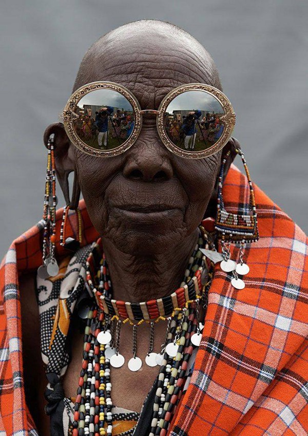 A woman in traditional Masai clothing wears large glamorous sunglasses.