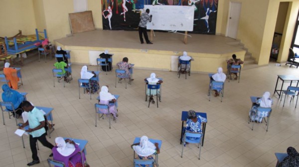 A classroom with pupils at desks, paying attention to a teacher writing on a whiteboard.