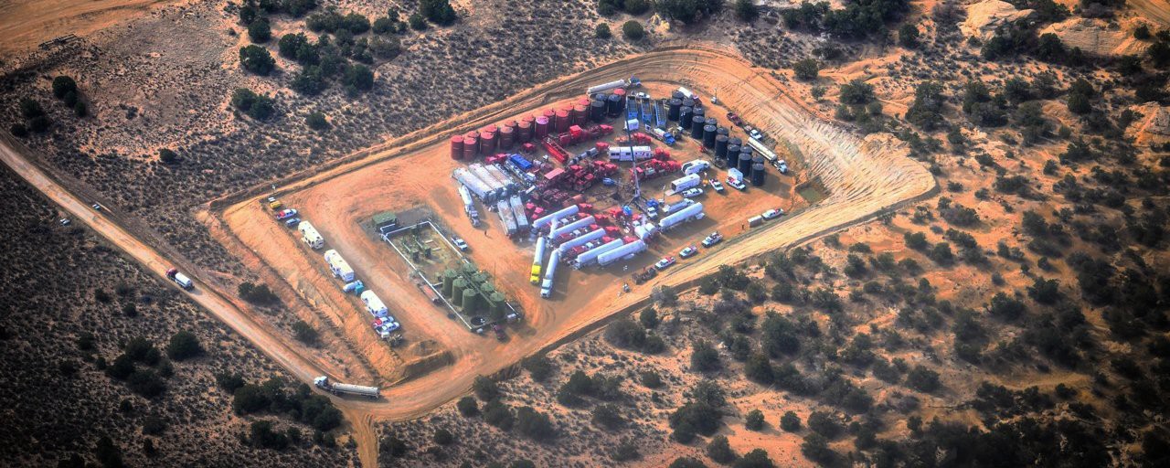 A fracking site, with a number of vehicles parkes in an open pit around fracking equipment.