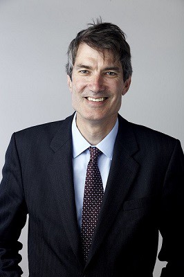 Steven Cowley smiles into the camera, while wearing a suit.