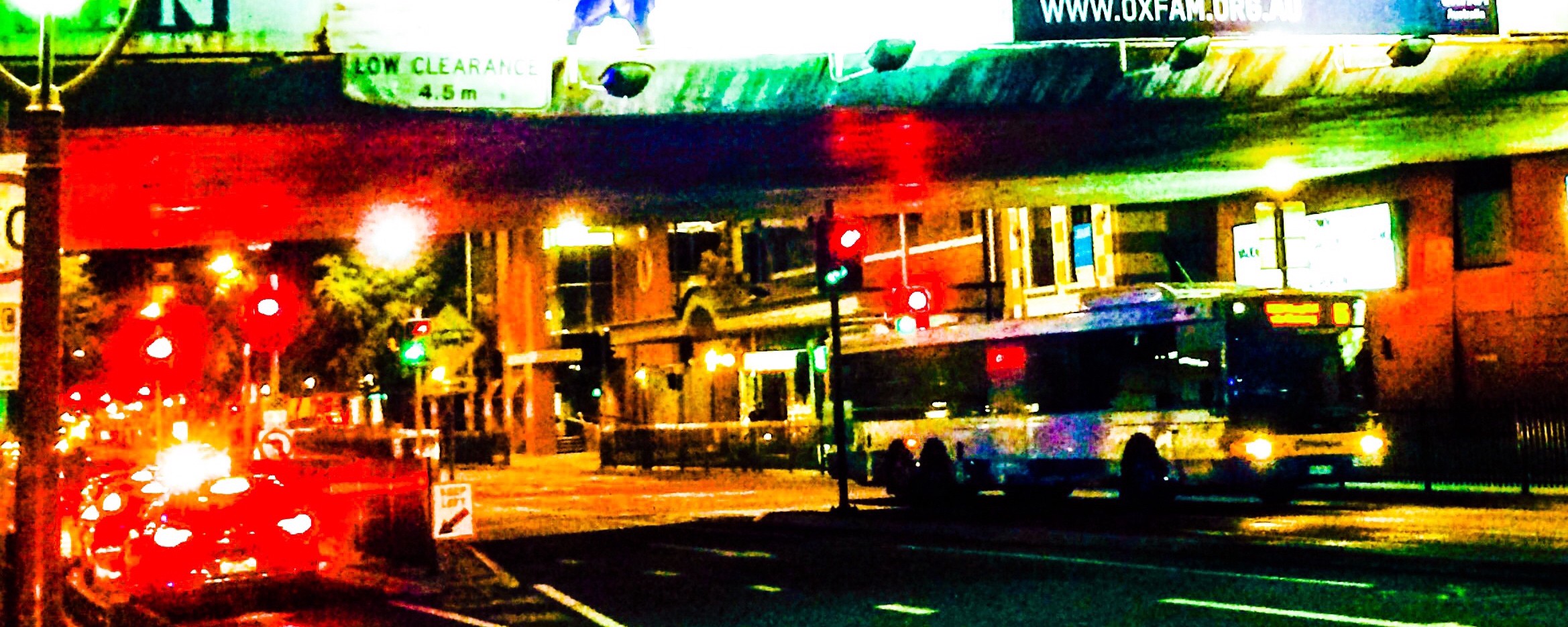 A street at night, with a bus waiting at an intersection.