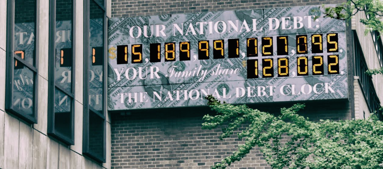 A large clock mounted on the wall of a building, displaying the US national debt. In the photo it's $15,189,991,727,095.