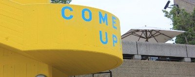 A concrete staircase painted yellow, with the words "come up" on it.