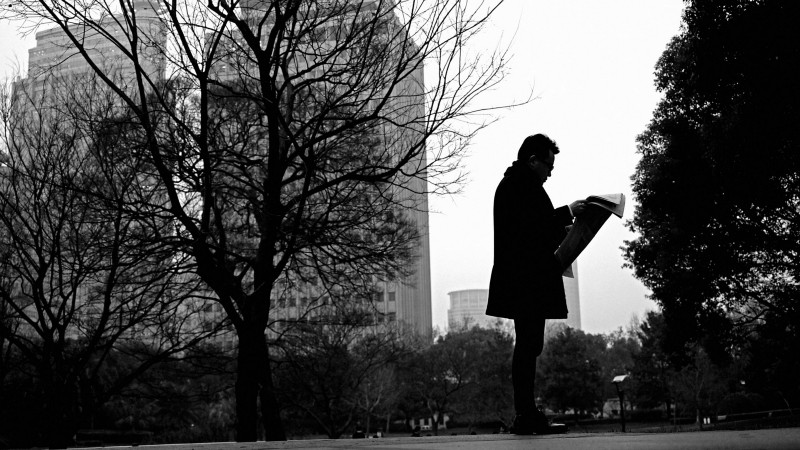 A person reading a newspaper in a park.