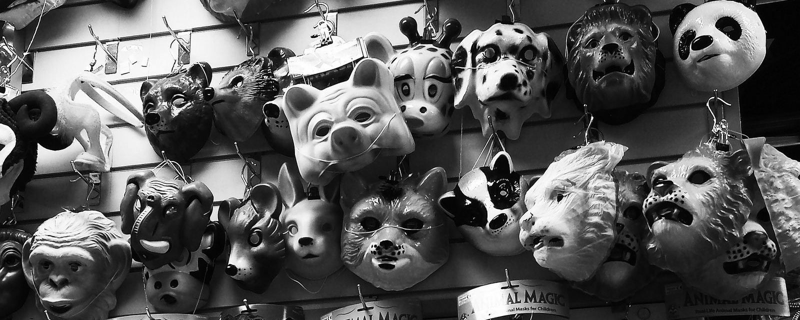 A wall of a store, with lines of plastic animal masks hanging from hooks.