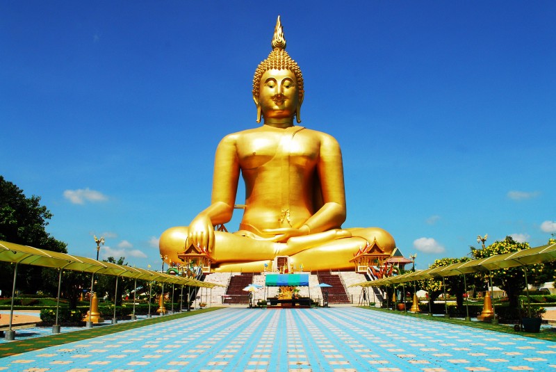 A large golden Buddha statue, sitting cross-legged in a courtyard.