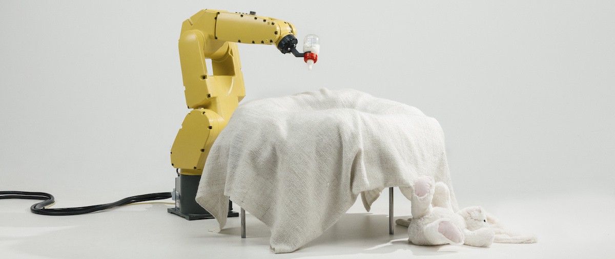 A robotic arm squeezes a baby's milk bottle over a crib.