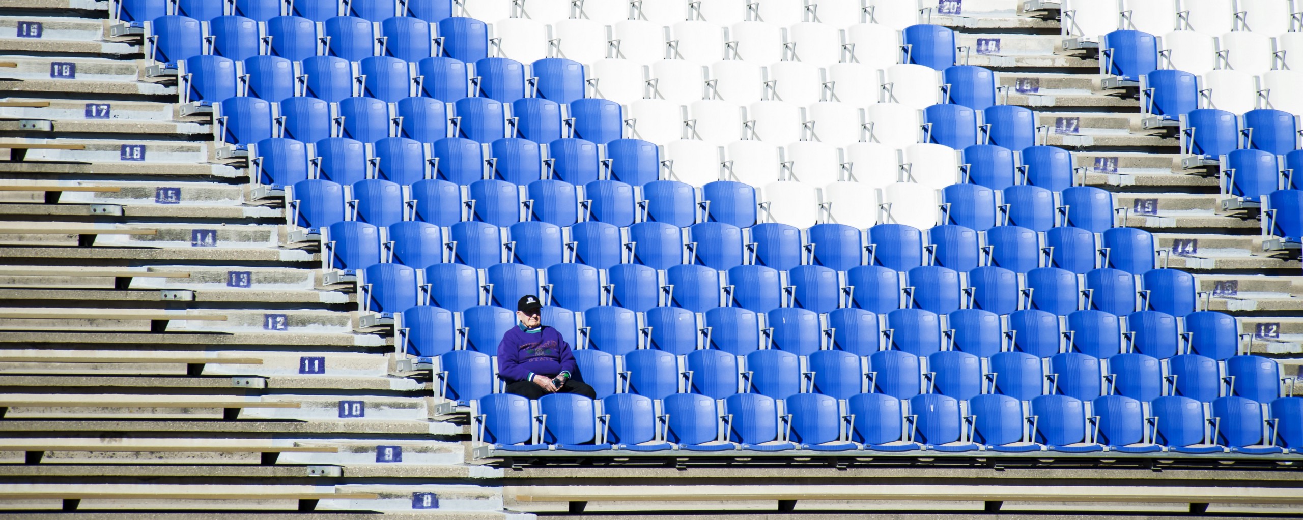 A man sits alone in his seat in an empty sports stadium.