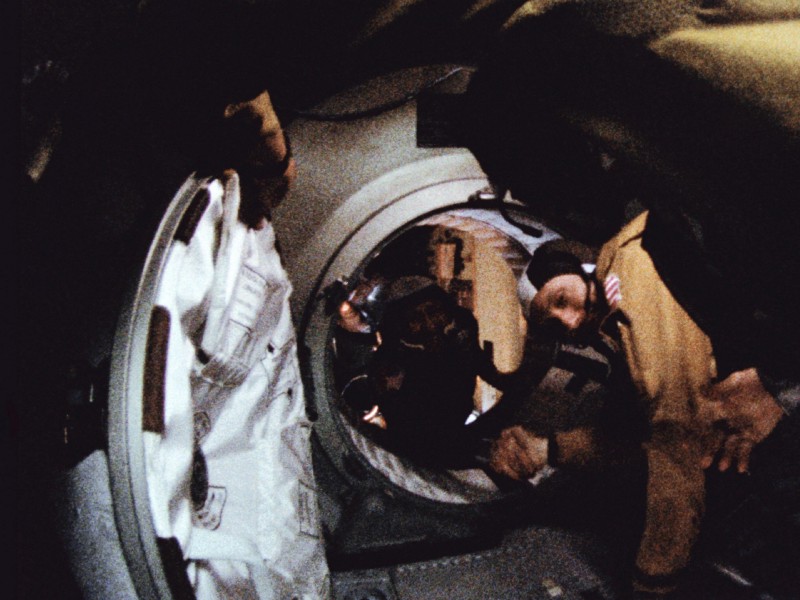 Two astronauts (or cosmonauts, if you're Russian) reach through an open hatch between two spacecraft to shake hands. They are smiling.