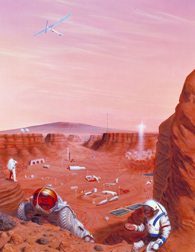 An astronaut stands next to their rover in the foreground, as they inspect a fossil in the red dirt of Mars. In the background, a surface base made up of a several white buildings. A rocket takes off in the far background.