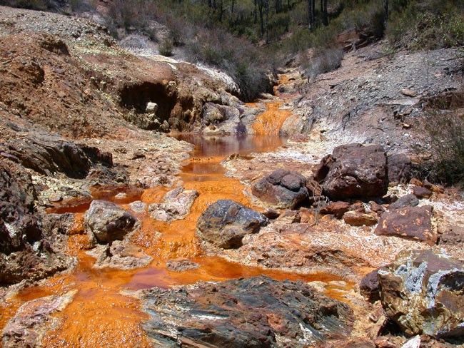 A river running along bare banks is bright orange and viscous.