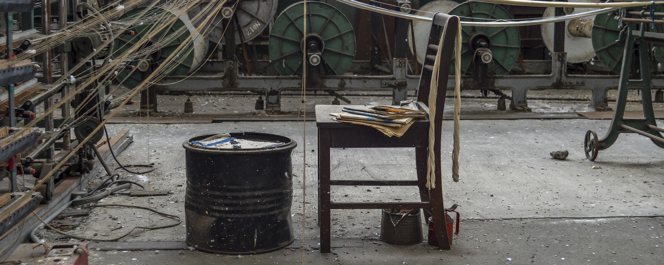 A wooden chair and an oil drum in a derelict textile workshop.