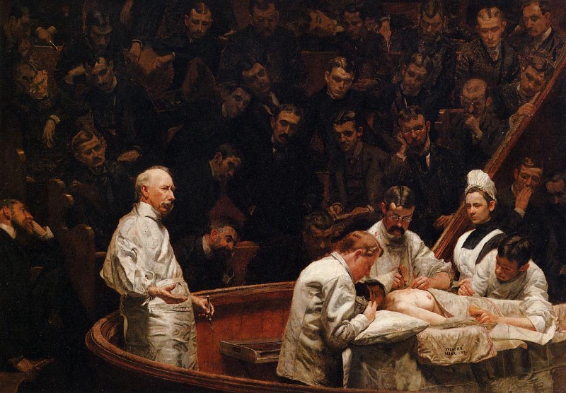 Open surgery in a lecture theater, with doctors wearing white scrubs.
